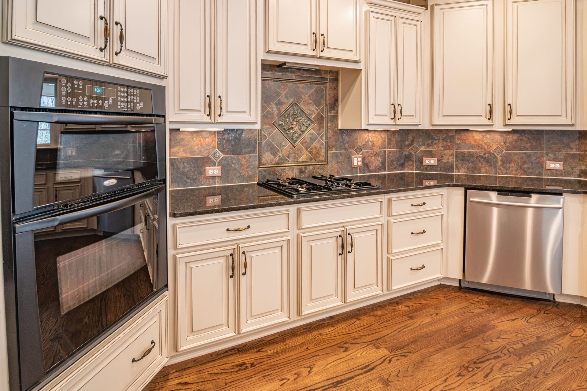 A modern kitchen featuring cabinets, a dishwasher, and a double oven with hardwood floors.