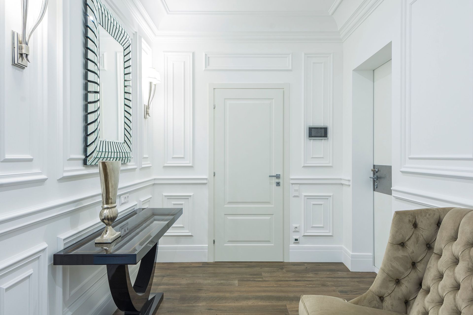 Sophisticated white interior with classic moldings and minimalist design, featuring a stylish mirrored wall and cozy seating.